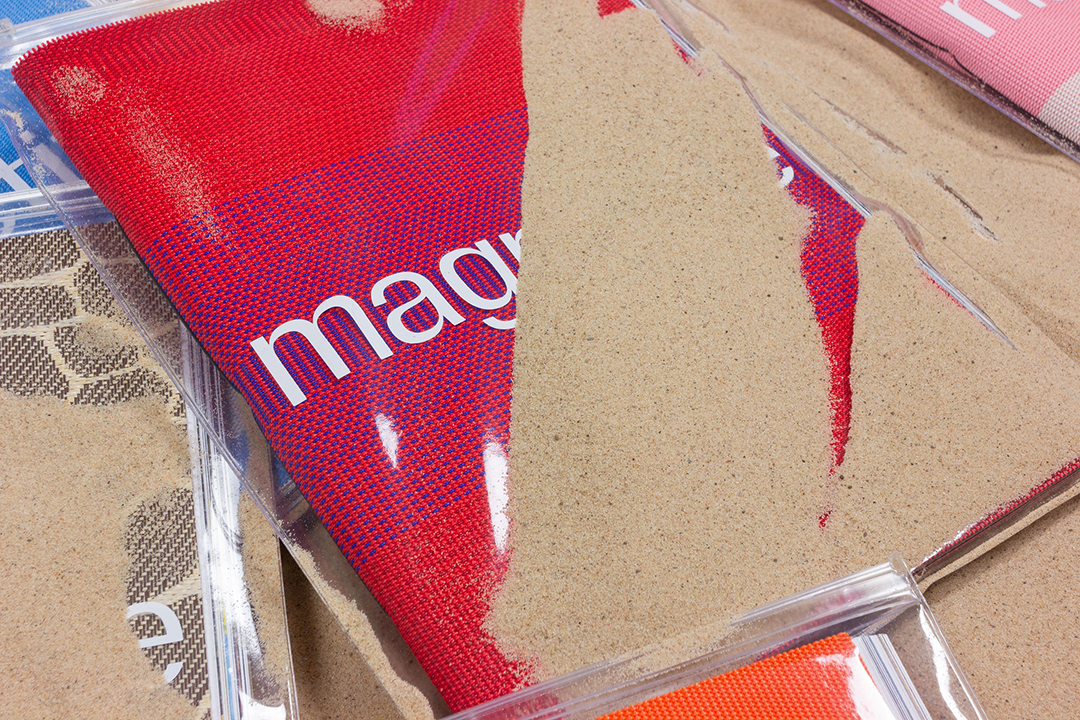 Premium printed magazone with textured recycled textile cover partially covered in sand, sustainable print London