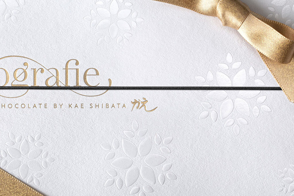 Luxury packaging with blind embossed floral patterns, gold foil lettering, and textured white paper stock